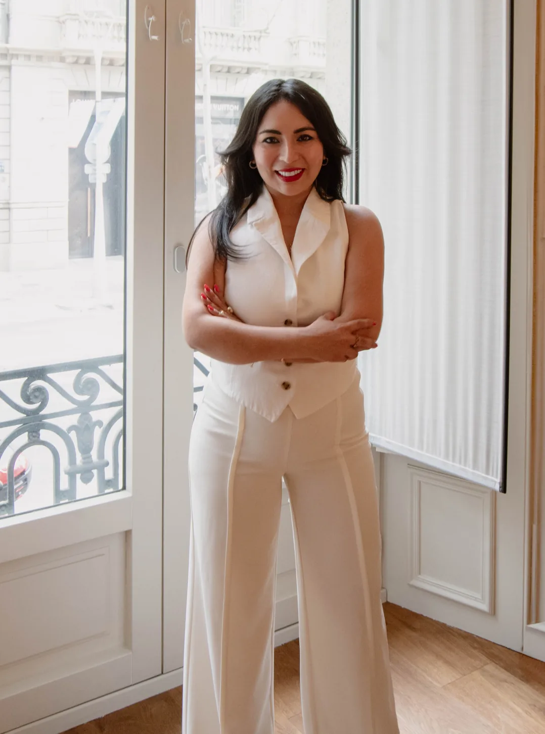 Narda Arias — Historia Narda Arias de pie con traje blanco junto a una ventana